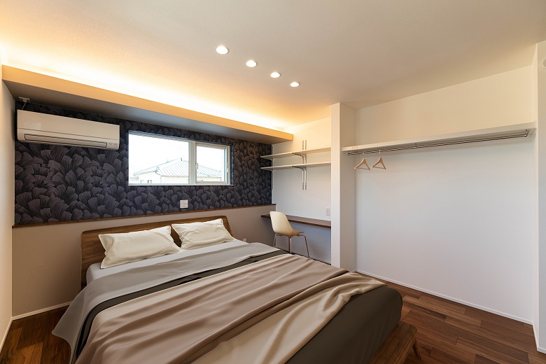 柄のあるシックなアクセントクロスに間接照明を合わせた落ち着く寝室。壁側の収納にはあえて建具を設けず、片付けやすく・しまいやすい工夫
