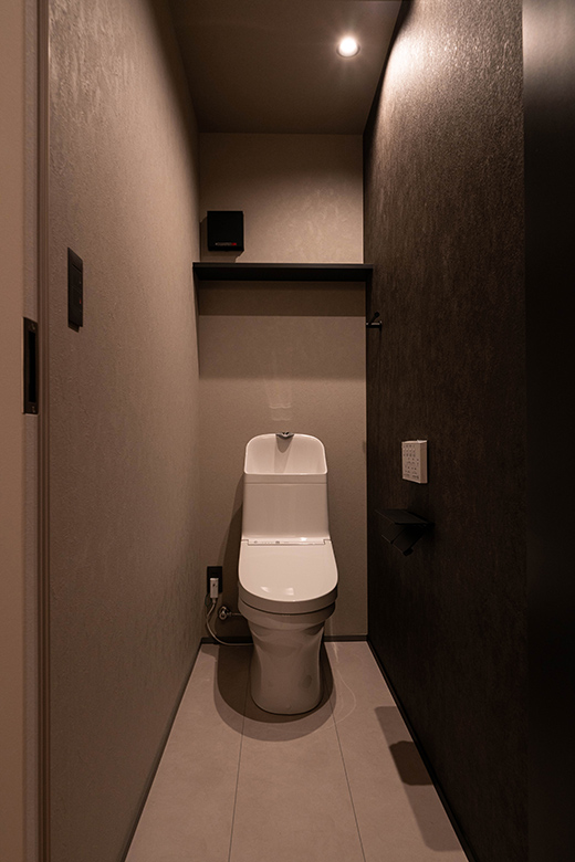 ダークトーンでまとめたトイレ空間。壁には質感のある素材を使い、シンプルながらも上質な雰囲気が漂う