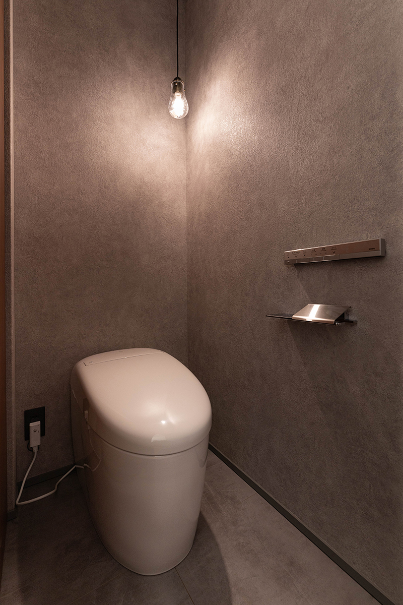 トイレは壁･床ともにモルタル柄を使い、シンプルなクリア電球によって洗練された印象がより引き立つ