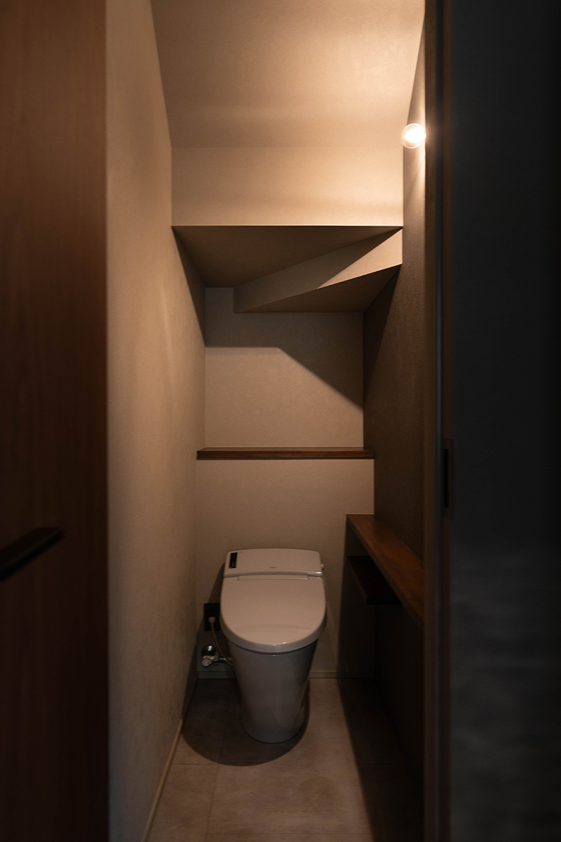 階段下を活用したトイレは、ブラケット照明1つだけで必要な明るさを確保。柔らかな光が陰影を生み、落ち着きのある雰囲気を作り出す