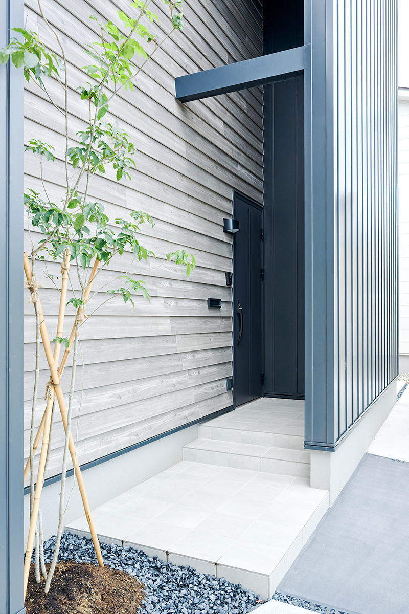 異素材の組み合わせが美しい玄関アプローチ。シンボルツリーのやわらかな緑がやさしく寄り添い、住まいに豊かな表情を添える