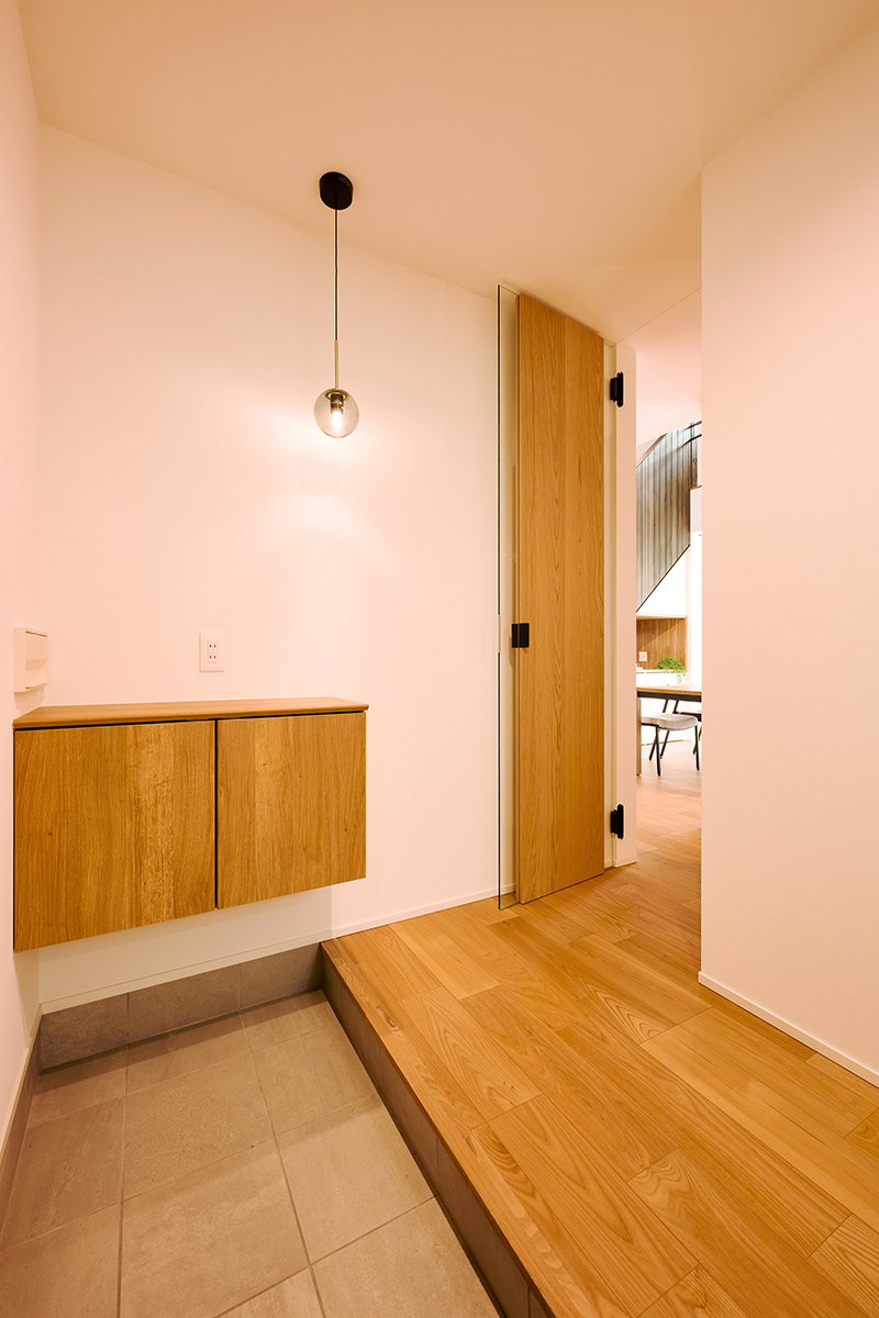 無駄を削ぎ落としたシンプルな玄関空間。素材感の異なるタイルと木の床が心地よいコントラストを生み出す