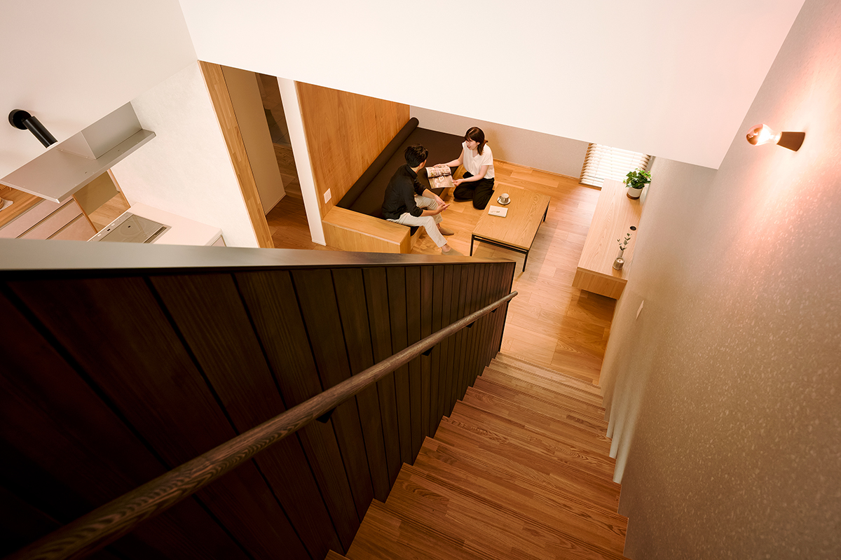 階段越しに覗く、木の温もりと心地よさが調和したリビング。造作ソファや木目の美しい床材が、空間全体に統一感をもたらす