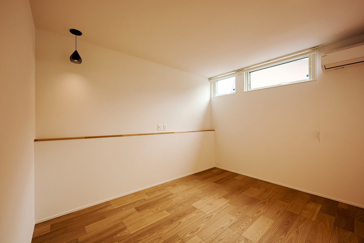 高窓から柔らかな光が差し込む、静かで落ち着いた寝室。最小限の照明とシンプルな設えが、心地よい眠りへと導く空間