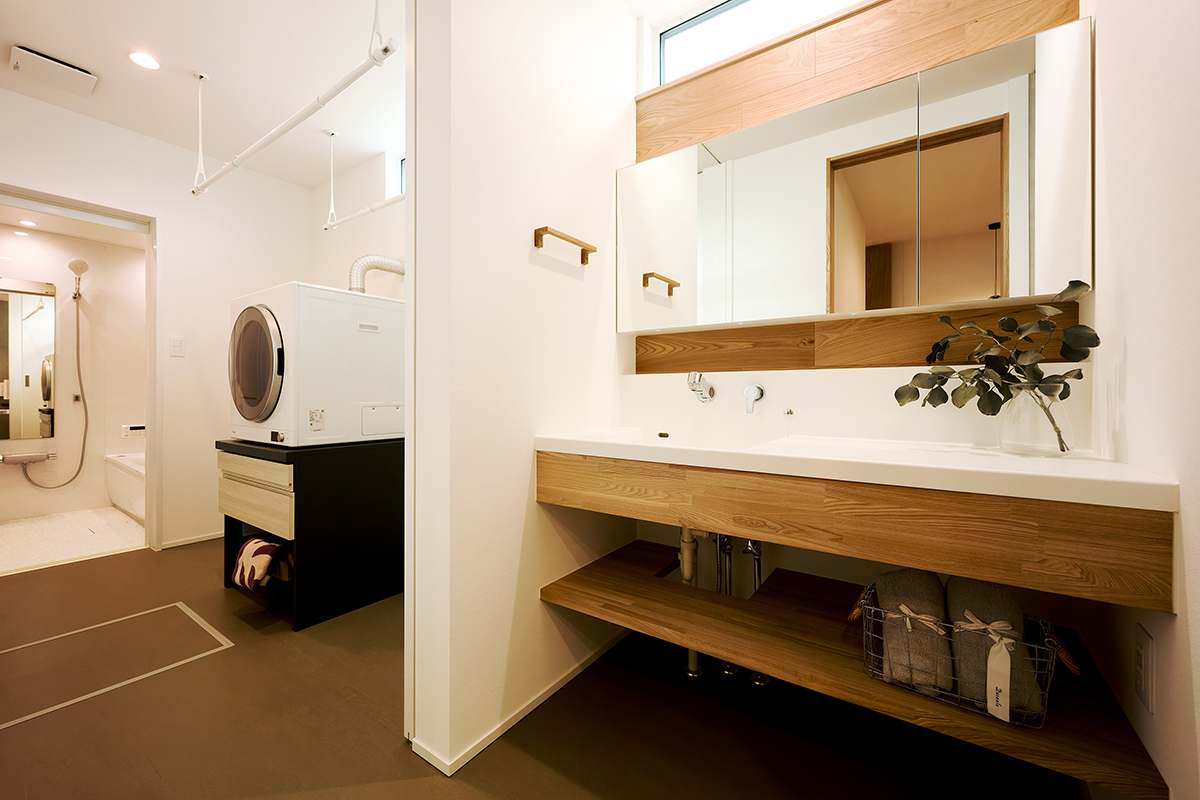 木の温もりと清潔感が調和した造作洗面台。横長のミラーが空間に広がりをもたらし、上部のハイサイドライトから柔らかな自然光が差し込む明るい洗面室