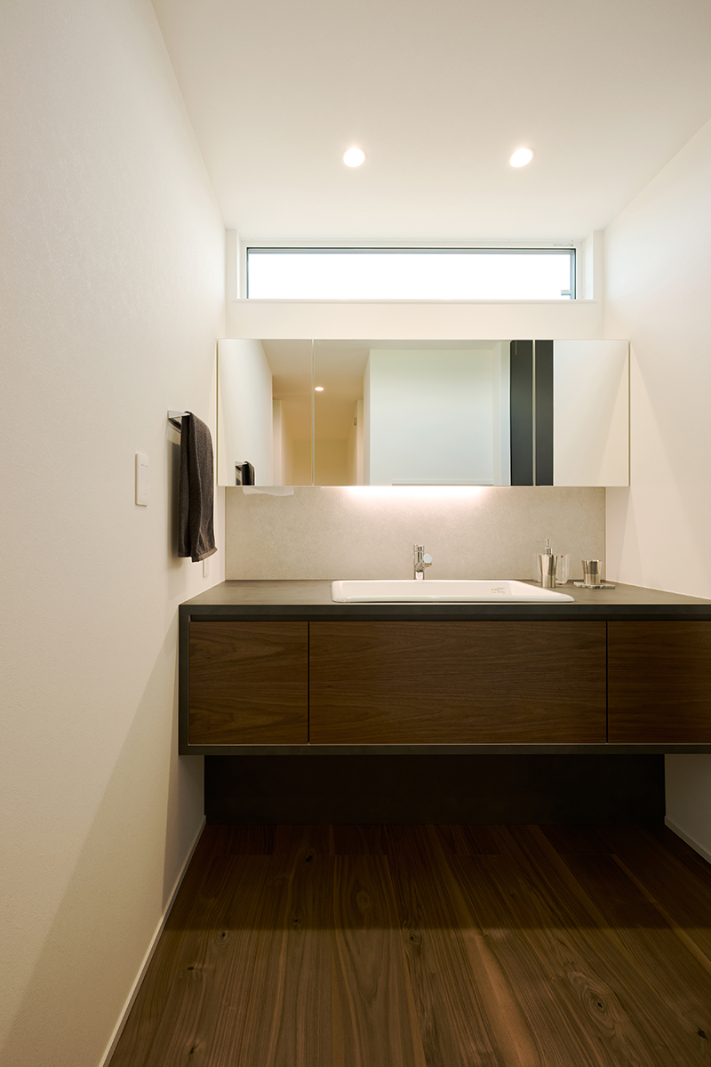 ウォールナット調の造作キャビネットと、手元を照らすやわらかな照明が調和した洗面