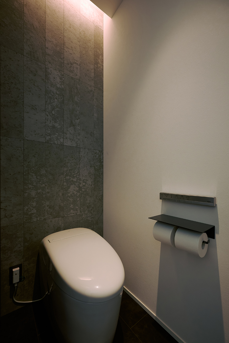 間接照明がタイル壁を柔らかく照らす、落ち着きのあるトイレ空間。シンプルながら上質な雰囲気を演出