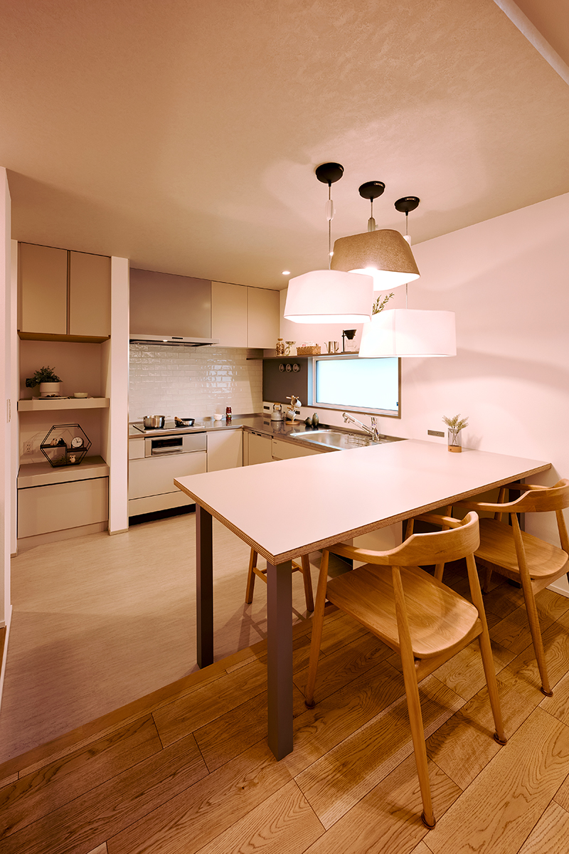 キッチンはコーナーを利用したL型のタイプで、隣接するダイニングとは床の素材と高さに変化をつけた。この間取りに合わせて設計された造作のダイニングテーブルと個性的な3つのペンダント照明が家族団らんに彩りを添える