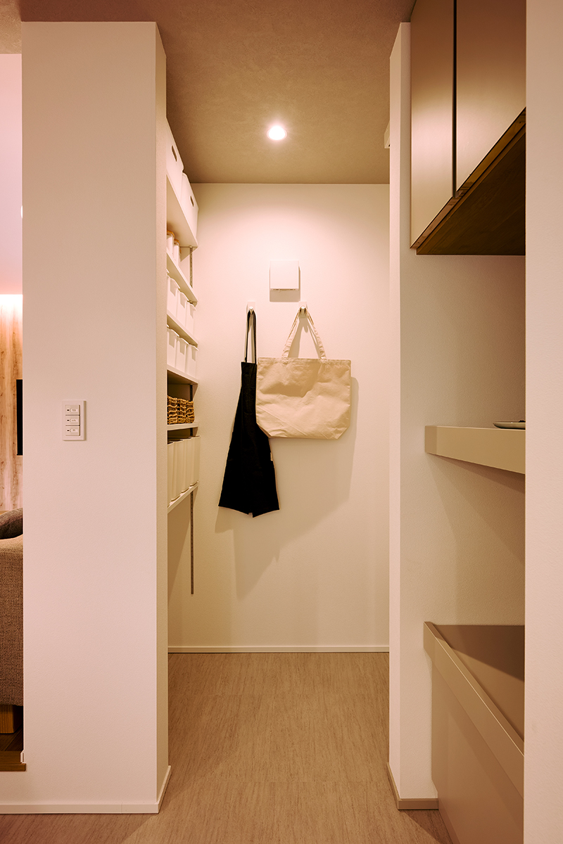 リビングからは死角になるキッチンの奥には可動棚を備えたパントリー。右側は冷蔵庫置き場で生活感を極力出さない間取り。手前にも家電などを置ける収納がある